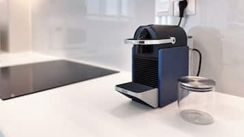 Una máquina de café con un recipiente de vidrio transparente a su lado, un enchufe y una encimera de cocina moderna.