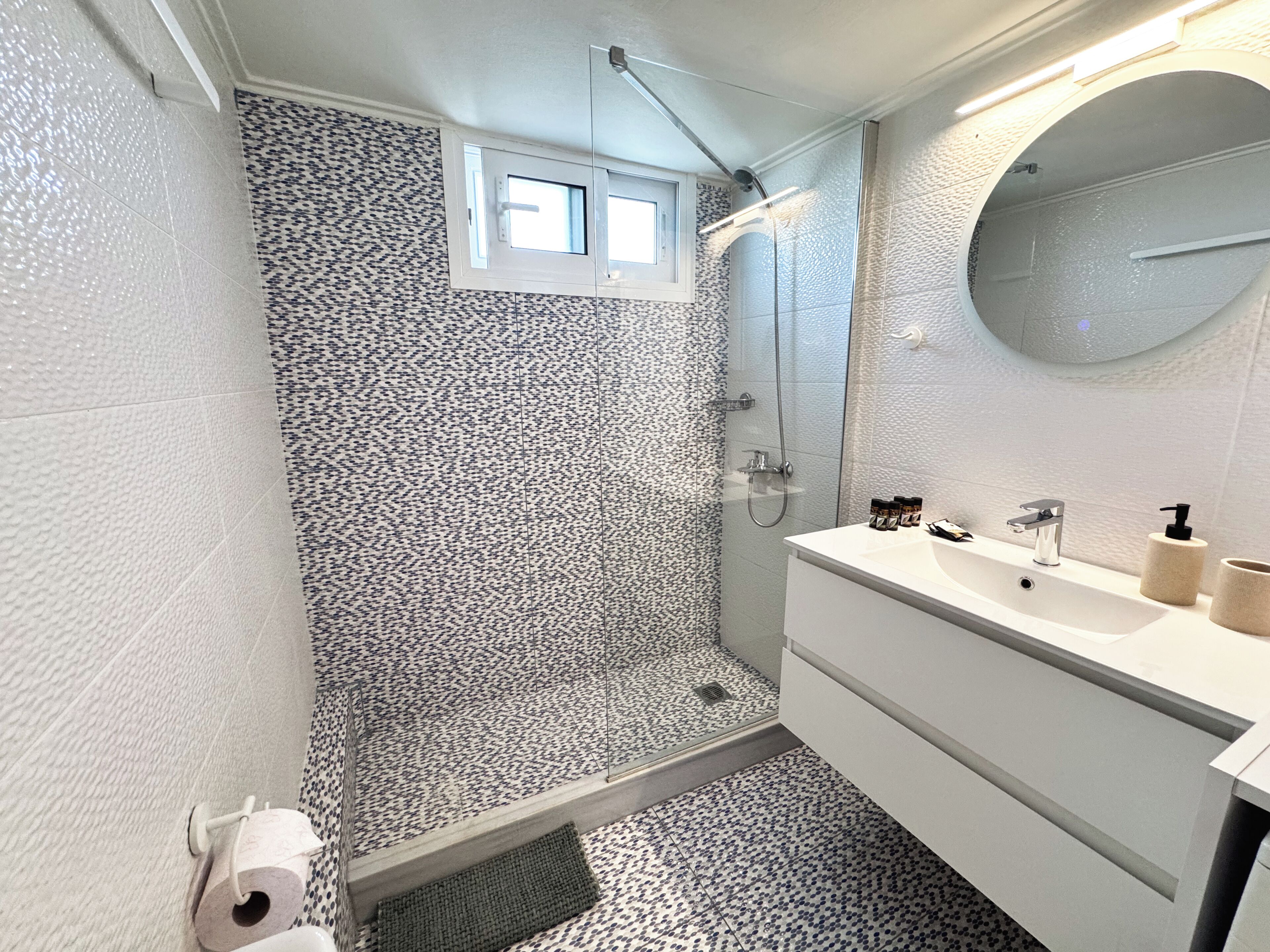 Baño con ducha, lavamanos con espejo y azulejos estampados.