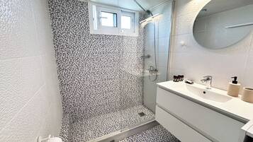 Baño con ducha, lavamanos con espejo y azulejos estampados.