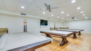 Ein Raum mit Billardtischen, Deckenventilatoren, eingelassener Beleuchtung und einem an der Wand befestigten Fernseher.