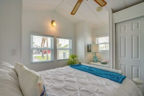 Ein Schlafzimmer mit einem Bett, zwei Fenstern, einem Deckenventilator, einem Nachttisch und einer Tür.