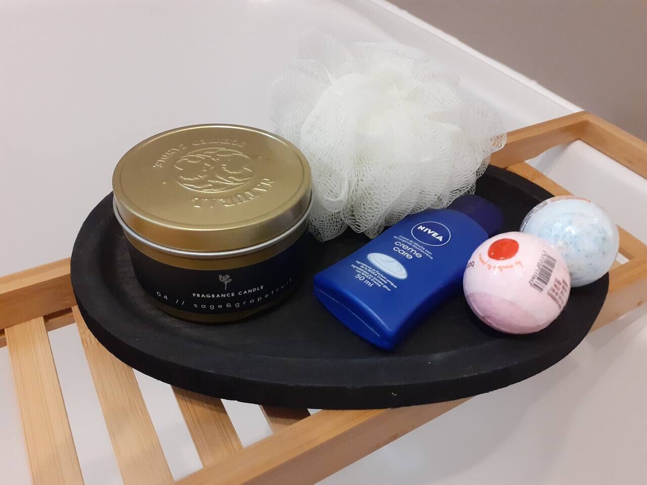 A tray with a fragrance candle, a white mesh, two toiletry items, and two balls of soap.
