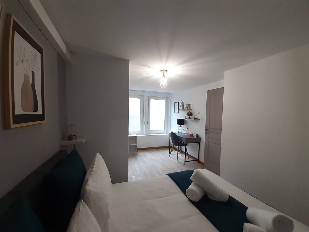 Une chambre à coucher avec un lit, un bureau et une chaise. Il y a une fenêtre qui laisse entrer la lumière naturelle et un luminaire au plafond.