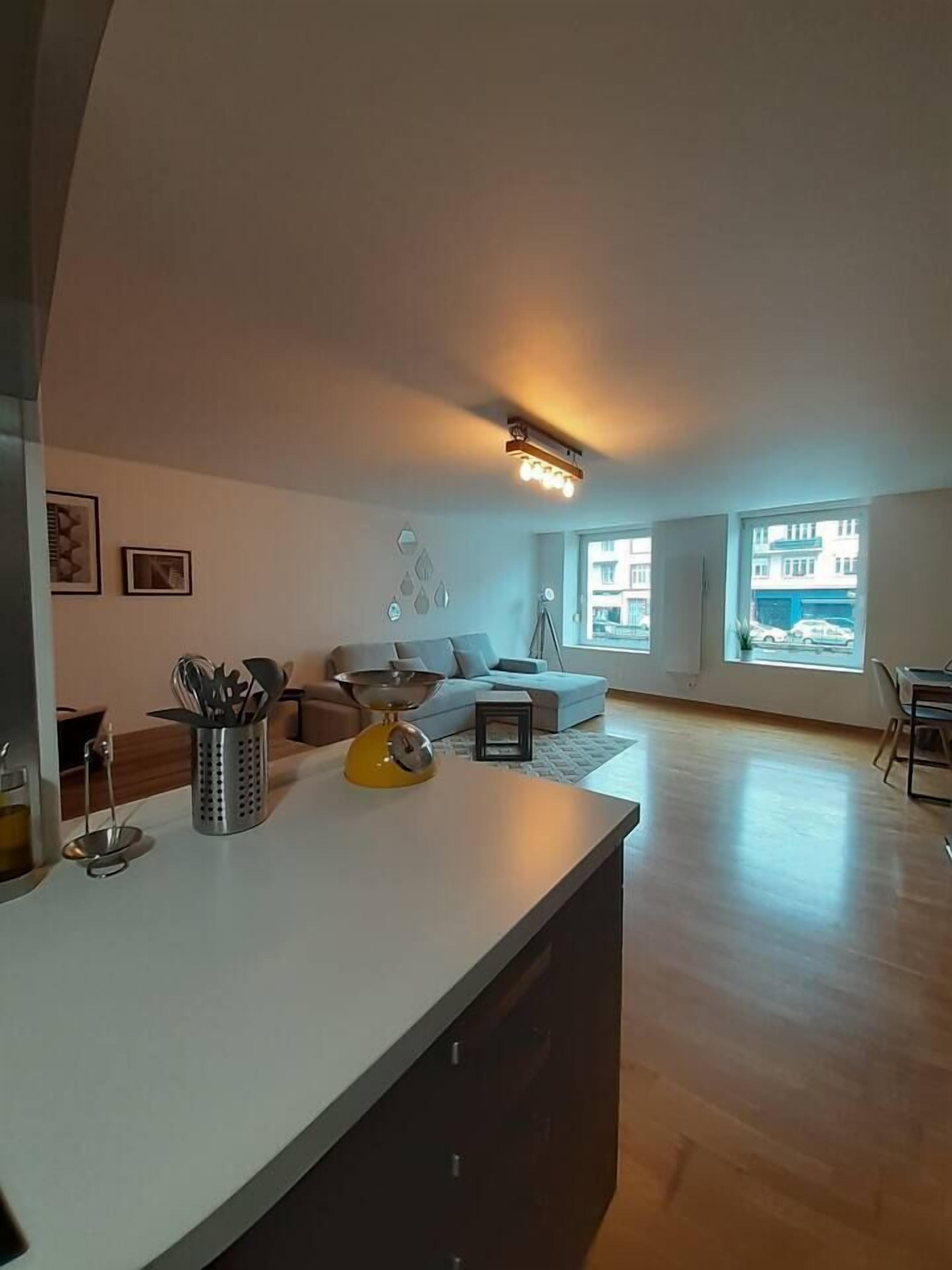 Una cocina moderna con encimera blanca, hervidor amarillo y zona de comedor con mesa y sillas.