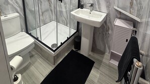 Un baño con ducha de vidrio, lavamanos blanco y paredes de mármol.