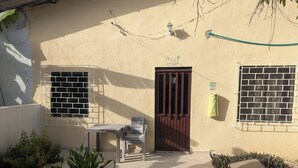 Una casa con patio empedrado, puerta de madera, ventanas con rejas y macetas con plantas.