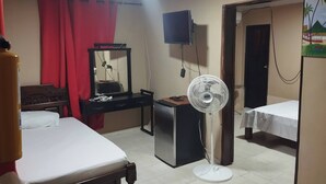 Habitación de hotel con cama, escritorio con computadora, televisor montado en la pared y ventilador de pie.