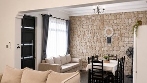 Un soggiorno moderno con un divano color beige, un'area pranzo con tavolo e sedie, e una parete in pietra.