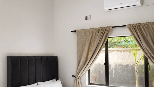 Una camera da letto con un letto, un comodino, una finestra con tende e un condizionatore.