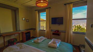 A hotel room with a bed, a television, a window with a city view, and a small table with a telephone.