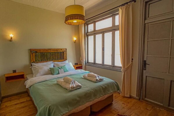 Una cama con cabecera, mesitas de noche, una ventana con cortinas y una puerta.