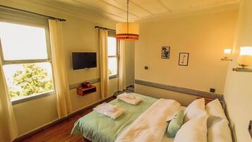 Une chambre d’hôtel avec un lit, un téléviseur fixé au mur et une fenêtre avec des rideaux.