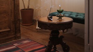 Ein Zimmer mit einem Holzkabinett, einer Topfpflanze, einem runden Tisch mit einem Dekorationsgegenstand und einem grünen, gepolsterten Sofa.