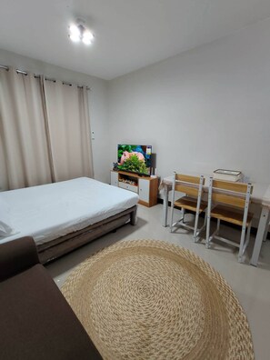 A bedroom with a bed, a TV, a desk with a chair, and a woven rug. - Homey Restful Stay at Saekyung Condominium (Lapu-Lapu)