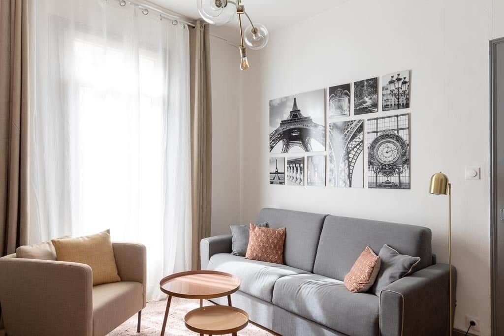 Een moderne woonkamer met een grijze bank, een beige fauteuil en een kleine ronde tafel.