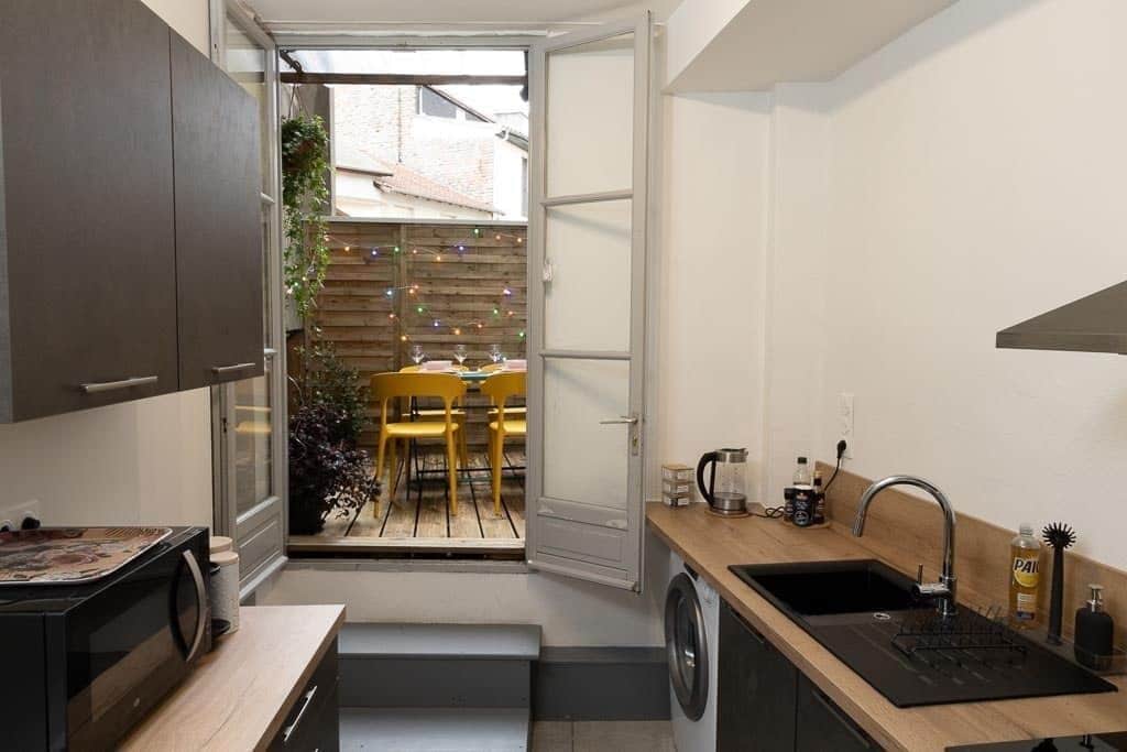 A compact kitchen with a washing machine, a sink, and a dining area visible through an open door.