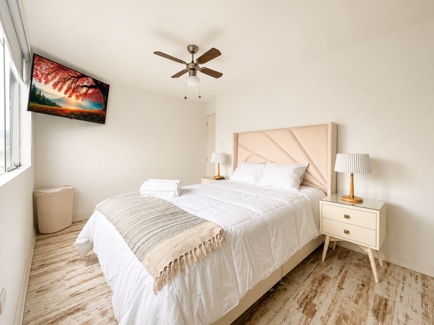 Un dormitorio con cama, ventilador de techo, mesita de noche, lámpara, radiador y un cuadro en la pared.
