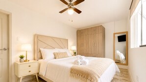 A bedroom with a bed, bedside tables, a ceiling fan, a wardrobe, and a mirror.