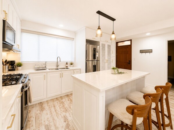 A modern kitchen with white cabinetry, a central island with bar stools, stainless steel appliances, and pendant lighting.