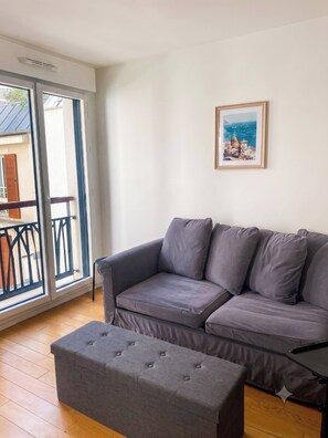 A grey sofa, a grey ottoman, and a framed picture on a wall. - Charming Studio in the Heart of Paris - Ideal for Couples (Paris)