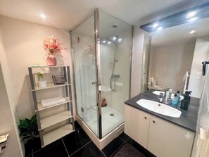 A modern bathroom with a glass-enclosed shower, a vanity with a sink, and a shelf with toiletries. - Charming Studio in the Heart of Paris - Ideal for Couples (Paris)