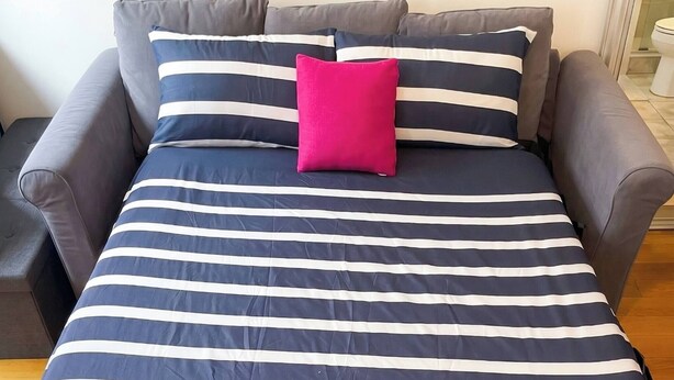 Una cama con una colcha a rayas y una almohada rosa brillante.