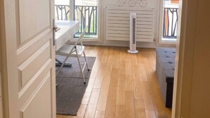 Una habitación con piso de madera, un radiador blanco, una mesa con sillas y una ventana con vistas al exterior.