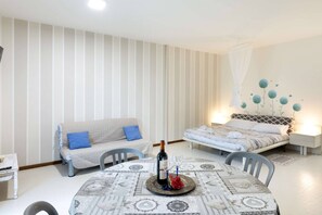 A room with a bed, a sofa, a dining table with a placemat, and a wall with a decorative design. - Charming Studio Apartment with Ocean View in Riccione (Riccione)