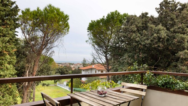 Een balkon met een houten tafel en stoelen, met uitzicht op een tuin en huizen.