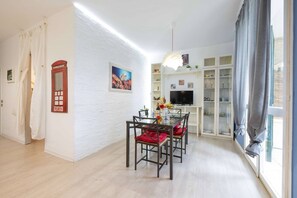 Ein modernes Wohnzimmer mit Essbereich, weißen Ziegelwänden, einem roten Telefon und einem Fernseher auf einem weißen Schrank.