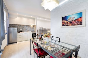 A modern kitchen with white cabinets, a stainless steel refrigerator, and a dining area with a glass table and red cushions. - Charming Modern Loft with Sea View in Riccione Hills (Riccione)