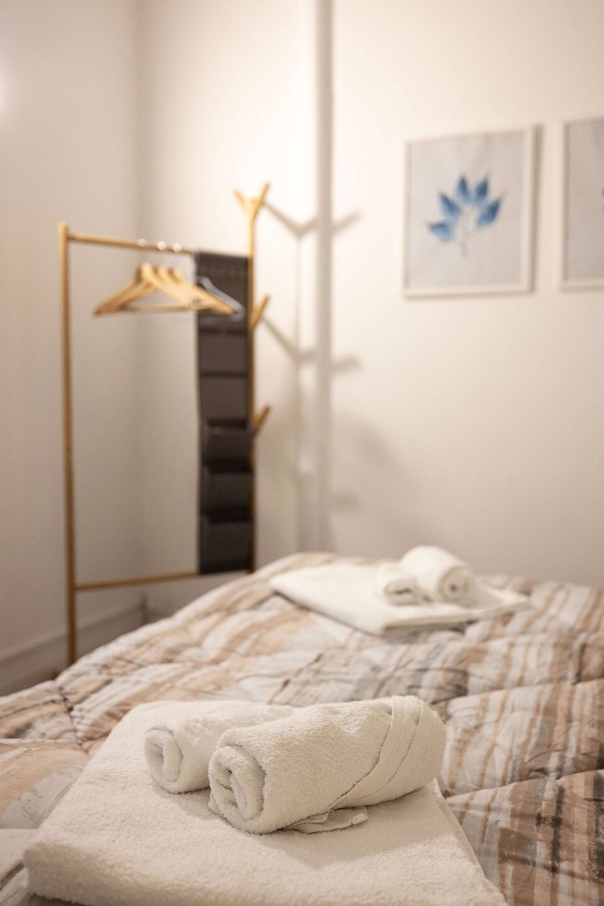 Une chambre d’hôtel avec un lit, une serviette, un porte-vêtements et un tableau encadré au mur.