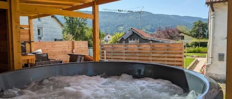Ein Whirlpool mit Holzüberdachung, im Hintergrund Häuser und Berge.
