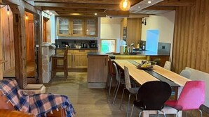 A cozy interior with a dining area, wooden ceiling, and a kitchen in the background. - Le Vosgien: Group Lodging (Saulxures-sur-Moselotte)