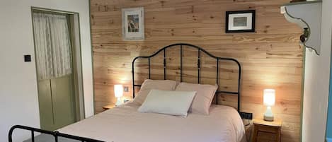 A bedroom with a wooden wall panel, a metal bed frame, two bedside lamps, and a hanging light fixture.