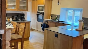 A kitchen with wooden cabinets, a central island, and a dining area with chairs. - Le Vosgien: Group Lodging (Saulxures-sur-Moselotte)