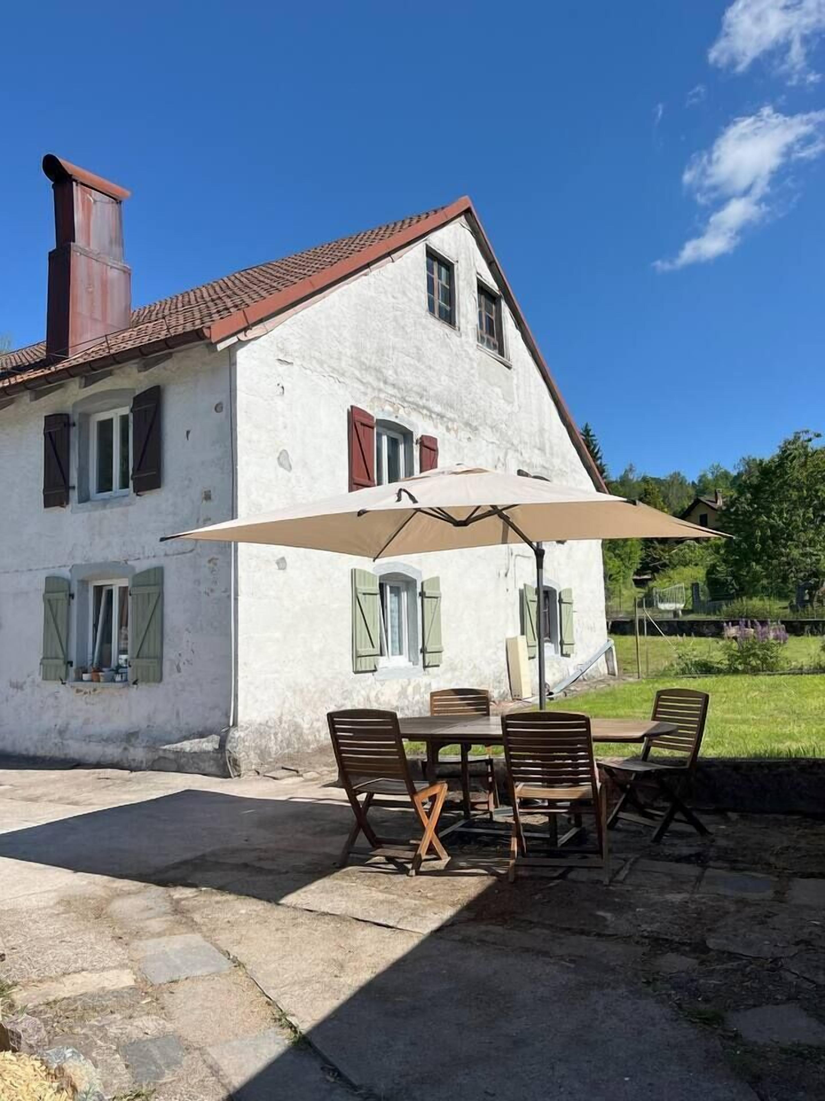 Un bâtiment blanc avec un toit rouge, une cheminée et une terrasse avec une table et des chaises.