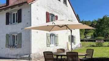 Un bâtiment blanc avec un toit rouge, une cheminée et une terrasse avec une table et des chaises.