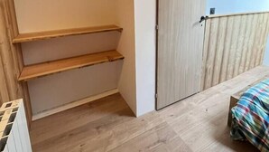 A room with a wooden floor, a bed with a colorful blanket, a wooden door, and a wall-mounted light fixture. - Le Vosgien: Group Lodging (Saulxures-sur-Moselotte)