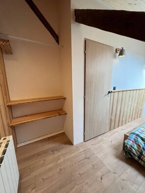 Una habitación con piso de madera, una cama con una manta colorida, una puerta de madera y un aplique de pared.