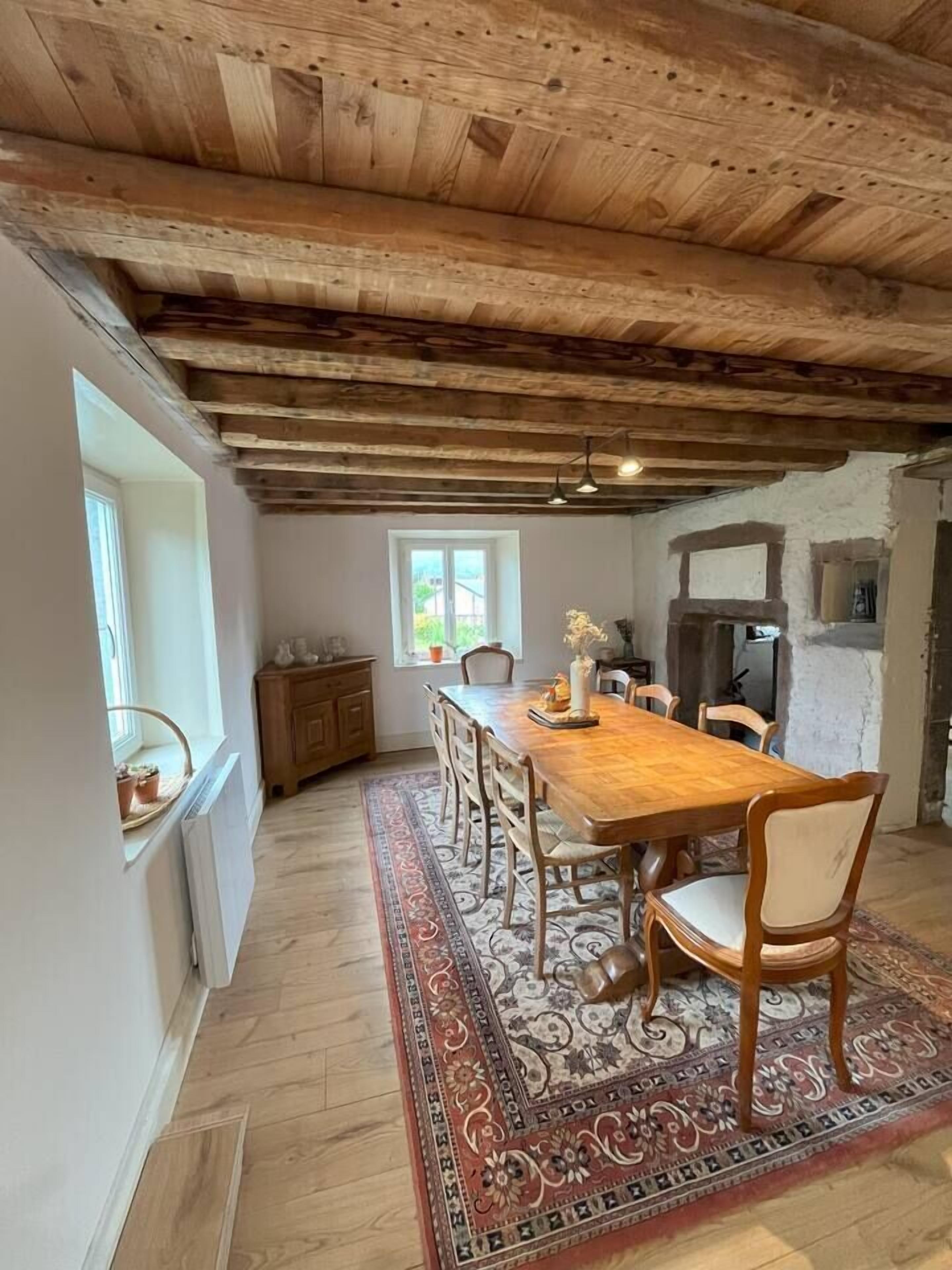 Un coin repas avec une table en bois, des chaises, un tapis et une cheminée.