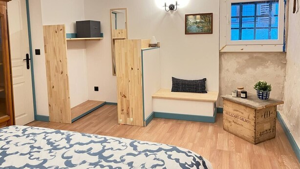 A bedroom with a bed, a bench, a wooden crate with bottles, a wall-mounted light, and a window. - Le Vosgien: Group Lodging (Saulxures-sur-Moselotte)