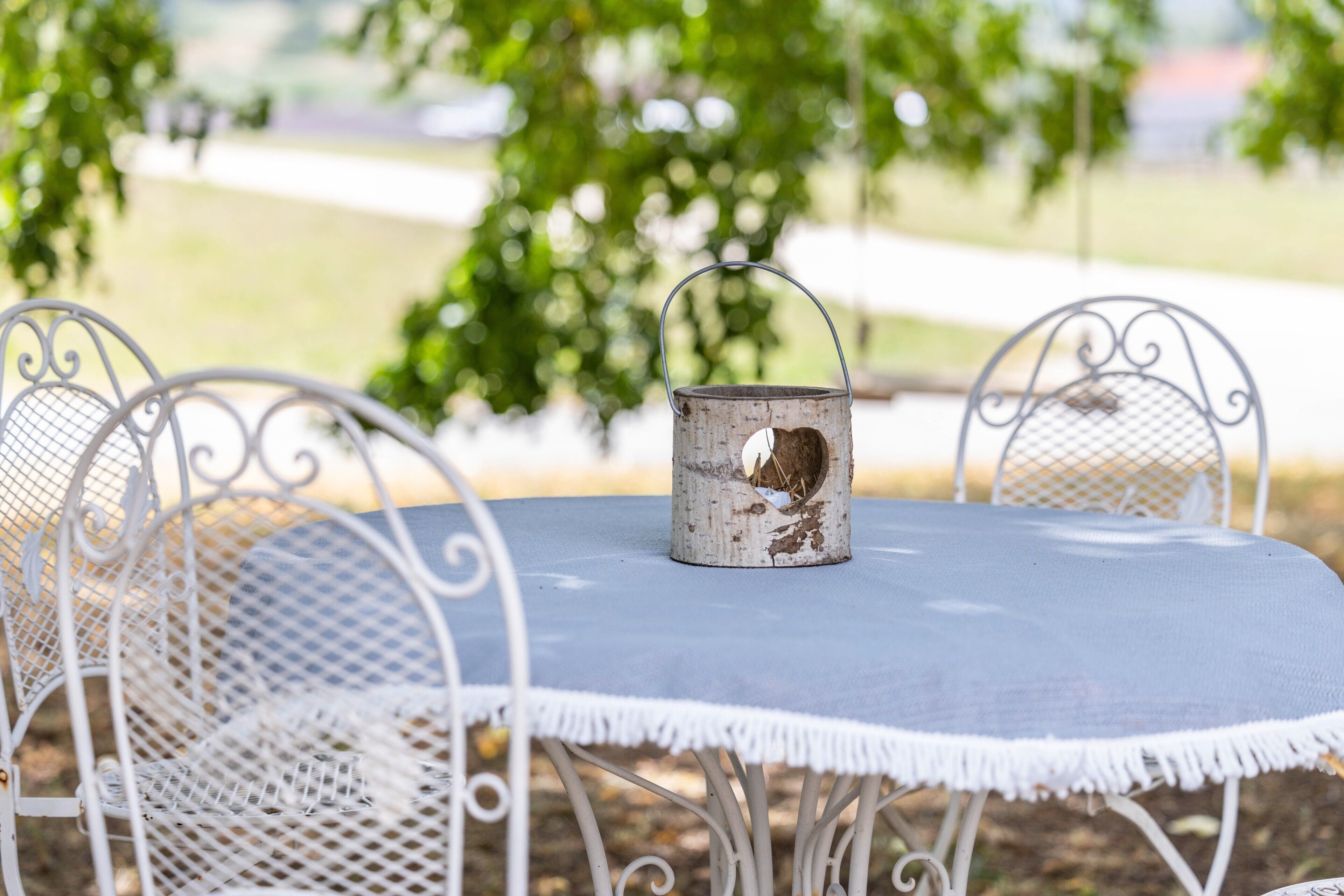 A metal table with a white mesh chair, a metal bucket with a handle, and a blue tablecloth.