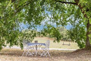 An outdoor seating area with a table and chairs under a tree, overlooking a natural landscape.