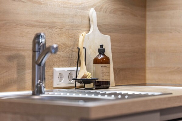 A kitchen sink with a soap dispenser and a wooden cutting board.