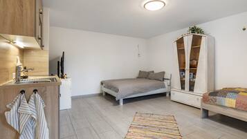 A compact bedroom with a bed, a small bedside table, a cabinet, and a kitchen area with a sink and a stove.