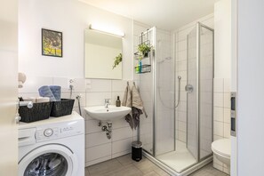 Ett modernt badrum med tvättmaskin, handfat, dusch med glasväggar och toalett.