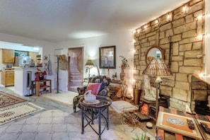 A cozy living room with a stone fireplace, a dining area with a kitchen in the background, and a patterned rug on the floor. - Walk to Parks & Dining! Lakewood Condo w/ Balcony (Lakewood)