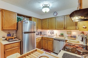 A kitchen with wooden cabinets, stainless steel appliances, a clock, and various kitchen items. - Walk to Parks & Dining! Lakewood Condo w/ Balcony (Lakewood)