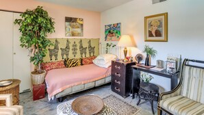 Een slaapkamer met een bed, een dressoir, een bureau, een stoel, een lamp, een potplant en kunstwerken aan de wanden.